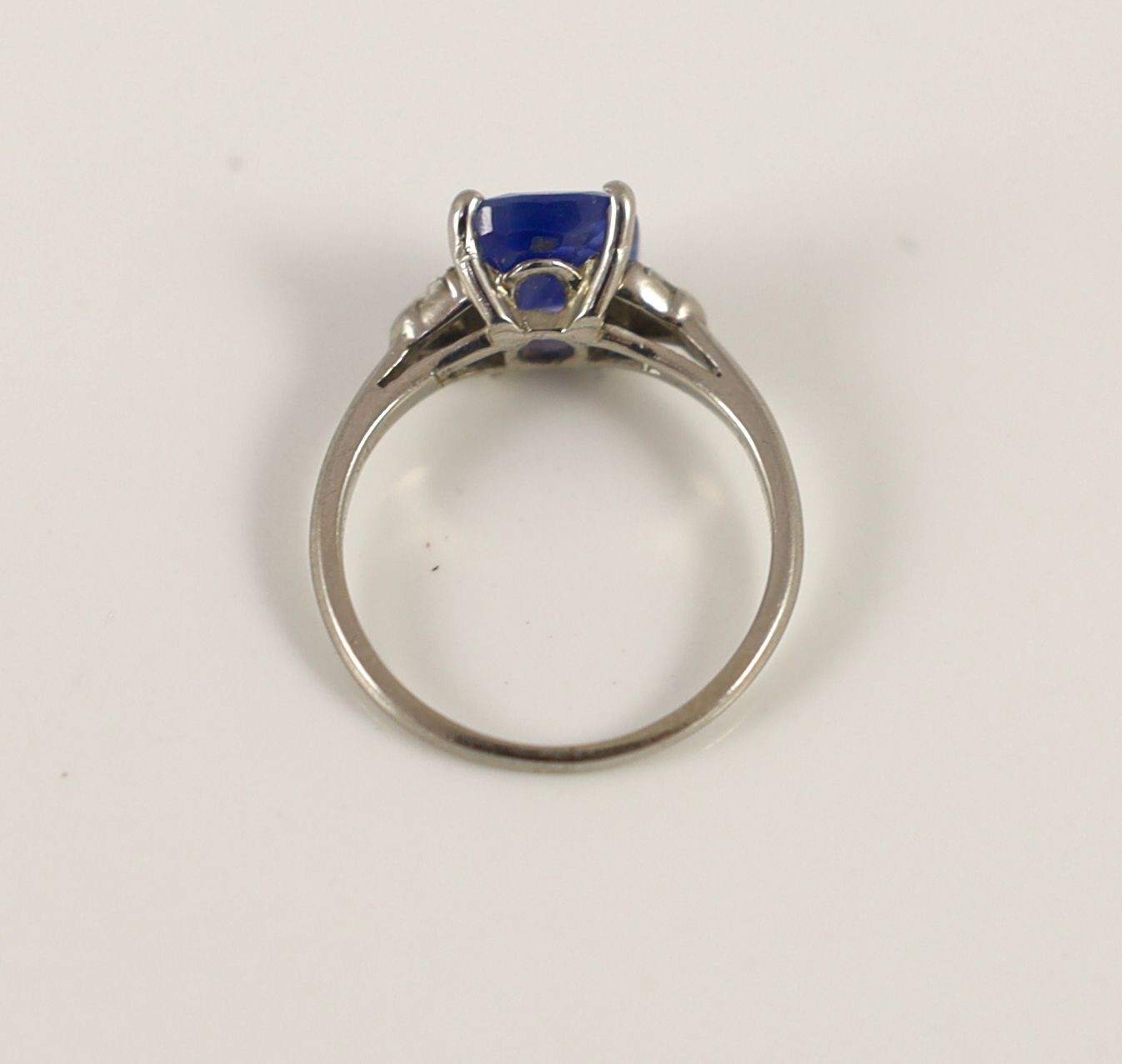 A platinum and palladium set single stone cushion cut sapphire ring, with triangular cut diamond set shoulders